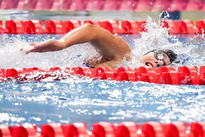 Ein Schwimmer, der eine Schwimmbrille und eine Badekappe trägt, nimmt an einem Freistilrennen teil und verursacht dabei Spritzer im Wasser, mit leuchtend roten Bahntrennern auf beiden Seiten.