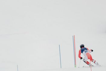 Ein Skifahrer mit rot-weißem Anzug und Helm, Nummer 32, fährt auf einer verschneiten Piste mit weißem, bedecktem Hintergrund durch Slalomstangen bergab.