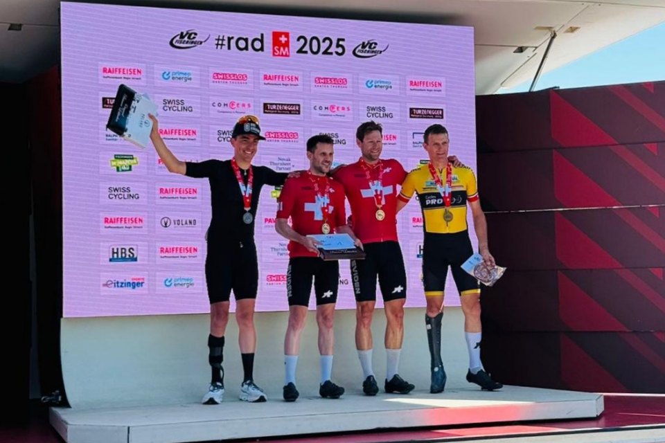Drei männliche Radfahrer stehen auf einem Podium bei einem Radrennen. Der mittlere und der linke Radfahrer tragen rote Schweizer Trikots und Medaillen, während der rechte Radfahrer ein gelbes Trikot trägt. Auf einem großen Bildschirm dahinter werden die #radSM 2025 und Sponsorenlogos angezeigt.