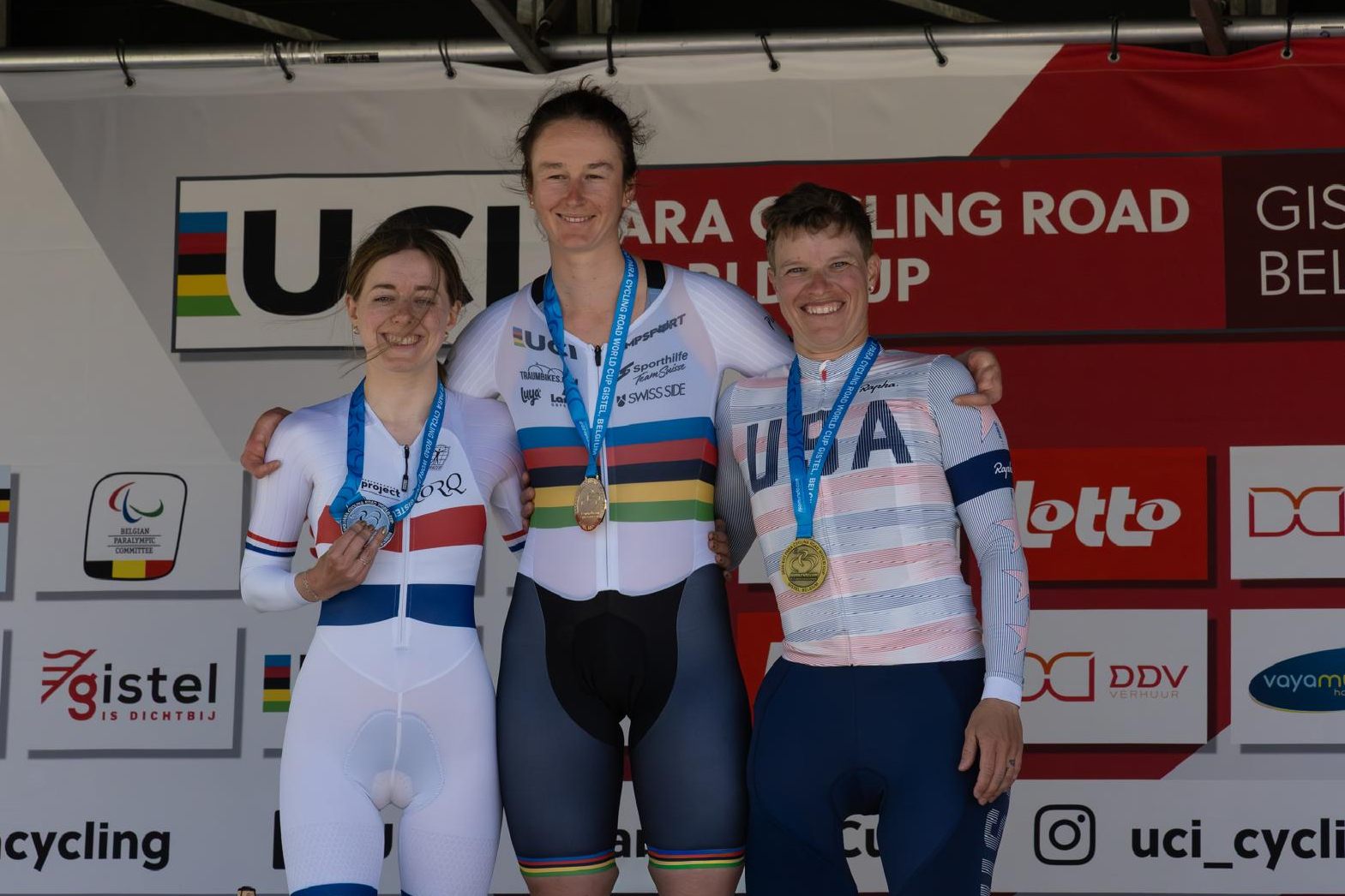 Drei Radsportlerinnen stehen auf einem Podium, jede trägt Medaillen und Radtrikots mit den Logos von FRA, SUI und USA. Sie lächeln unter einem UCI-Banner bei einer Straßenradsportveranstaltung.